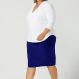 Side view of a classic capsule wardrobe staple - the white top. This V-neck , 3/4 sleeve, white bamboo jersey top is worn over a cobalt blue pencil skirt, worn untucked to show the shirttail hemline. Shown on a size 18, plus size woman, this classic top makes a great work blouse. Made in Australia by Australian andNew Zealand women's clothing brand, Leina & Fleur, this white jersey top is available to shop online in sizes 8 to 24