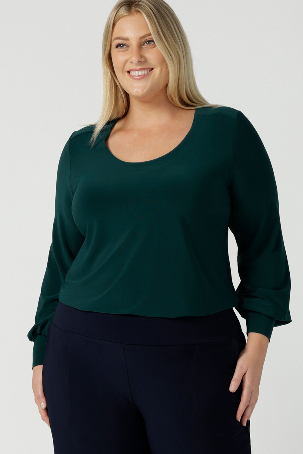 A size 18 woman wears the Jasper top in alpine. A scoop neckline design balloon sleeves and cuff detail. Made in Australia for women size 8-24. Styled back with Navy monroe pants. 