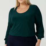 A size 18 woman wears the Jasper top in alpine. A scoop neckline design balloon sleeves and cuff detail. Made in Australia for women size 8-24. Styled back with Navy monroe pants. 