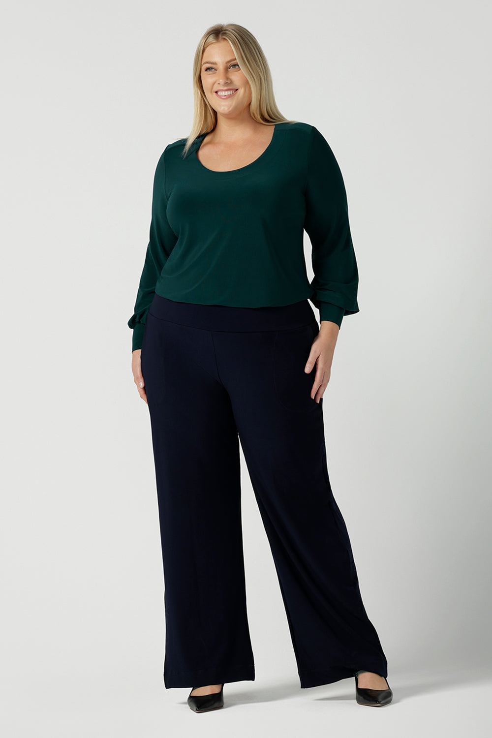 A size 18 woman wears the Jasper top in alpine. A scoop neckline design balloon sleeves and cuff detail. Made in Australia for women size 8-24. Styled back with Navy monroe pants.