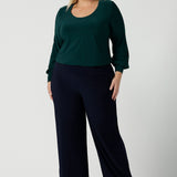 A size 18 woman wears the Jasper top in alpine. A scoop neckline design balloon sleeves and cuff detail. Made in Australia for women size 8-24. Styled back with Navy monroe pants.