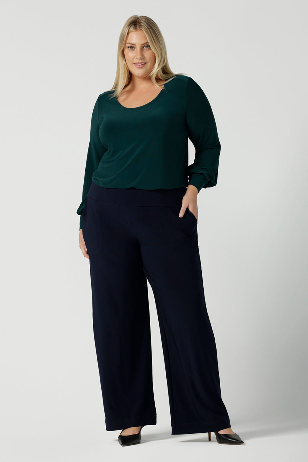 A size 18 woman wears the Jasper top in alpine. A scoop neckline design balloon sleeves and cuff detail. Made in Australia for women size 8-24. Styled back with Navy monroe pants.