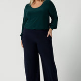 A size 18 woman wears the Jasper top in alpine. A scoop neckline design balloon sleeves and cuff detail. Made in Australia for women size 8-24. Styled back with Navy monroe pants.