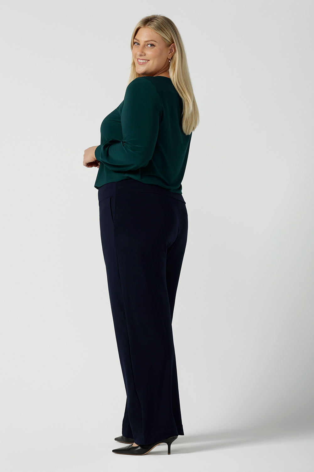 A size 18 woman wears the Jasper top in alpine. A scoop neckline design balloon sleeves and cuff detail. Made in Australia for women size 8-24. Styled back with Navy monroe pants.