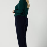 A size 18 woman wears the Jasper top in alpine. A scoop neckline design balloon sleeves and cuff detail. Made in Australia for women size 8-24. Styled back with Navy monroe pants.