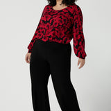 Front view of a size 18 woman wearing the scoop neck bold poppy top with balloon sleeves. Curved hemline and cuffed sleeves. Made in Australia for women size 8 - 24. Styled back with the Monroe pant in black, a straight leg comfortable corporate work pant.