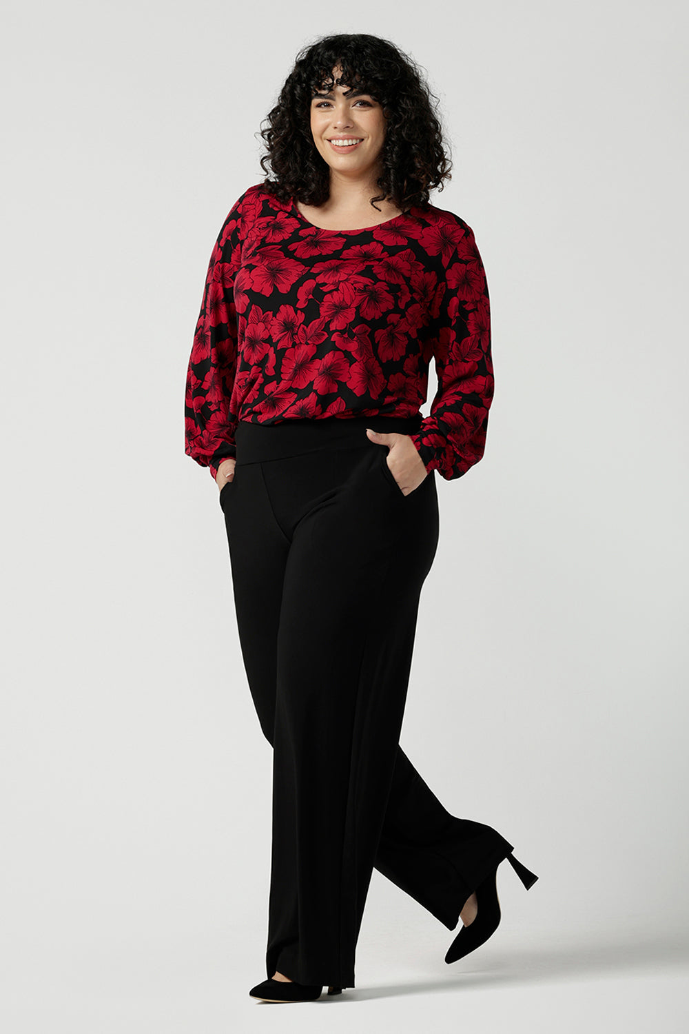 Front view of a size 18 woman wearing the scoop neck bold poppy top with balloon sleeves. Curved hemline and cuffed sleeves. Made in Australia for women size 8 - 24. Styled back with the Monroe pant in black, a straight leg comfortable corporate work pant.