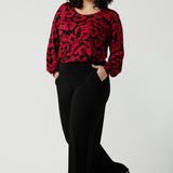 Front view of a size 18 woman wearing the scoop neck bold poppy top with balloon sleeves. Curved hemline and cuffed sleeves. Made in Australia for women size 8 - 24. Styled back with the Monroe pant in black, a straight leg comfortable corporate work pant.