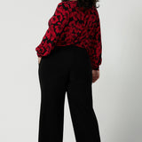 Back view of a size 18 woman wearing the scoop neck bold poppy top with balloon sleeves. Curved hemline and cuffed sleeves. Made in Australia for women size 8 - 24. Styled back with the Monroe pant in black, a straight leg comfortable corporate work pant.