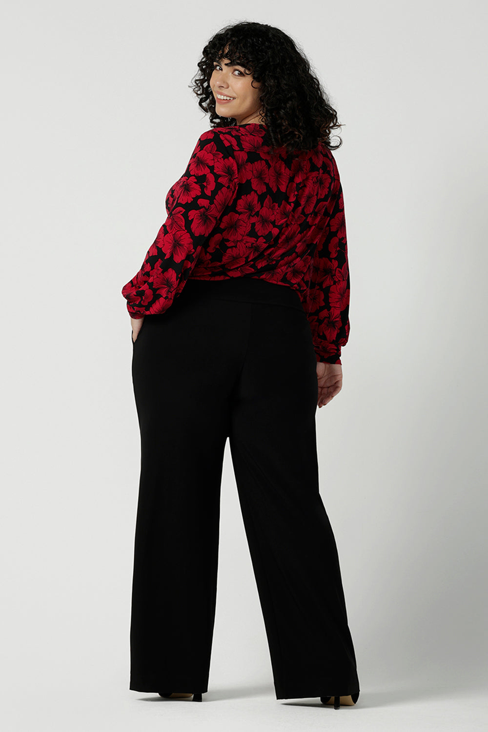 Back view of a size 18 woman wearing the scoop neck bold poppy top with balloon sleeves. Curved hemline and cuffed sleeves. Made in Australia for women size 8 - 24. Styled back with the Monroe pant in black, a straight leg comfortable corporate work pant.