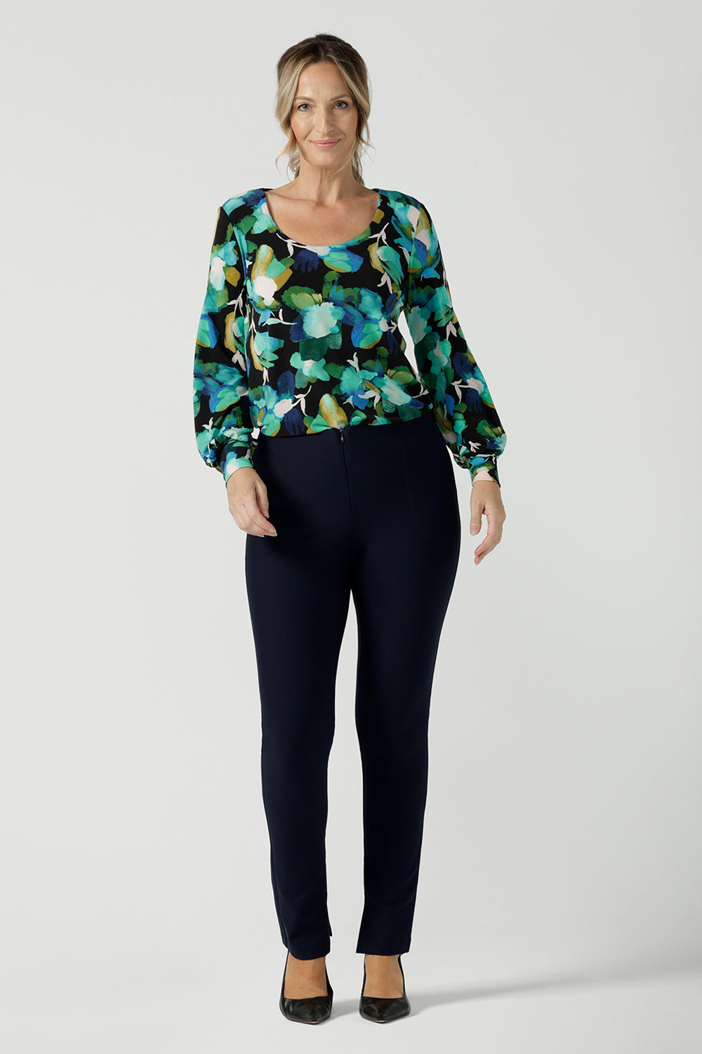 A size 8 woman wears the Jasper top in Canopy. A jersey style in a watercolour green print with balloon sleeves and cuff detail. Round neckline. Styled back with Navy Brooklyn pant in Navy. Made in Australia for women size 8 - 24.