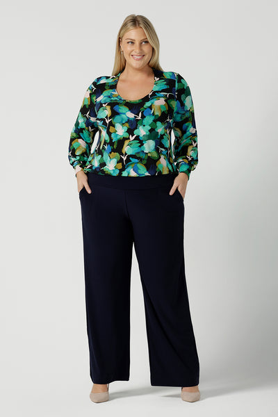 A size 18 woman wears the Jasper top in Canopy. A jersey style in a watercolour green print with balloon sleeves and cuff detail. Round neckline. Styled back with Navy Brooklyn pant in Navy. Made in Australia for women size 8 - 24.