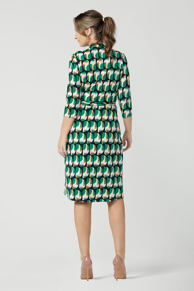 Back view of A size 10 woman wears a jersey wrap dress with 3/4 sleeves. In emerald geometric print jersey, this wrap dress is a good corporate dress for work wear capsule wardrobes. Shop Australian-made wrap dresses for work online is sizes 8 to 24.