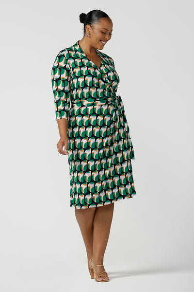 A size 18 woman wears a plus size jersey wrap dress with 3/4 sleeves. In emerald geometric print jersey, this wrap dress is a good corporate dress for work wear capsule wardrobes. Shop Australian-made wrap dresses for work online is sizes 8 to 24.