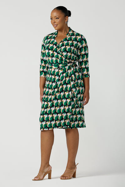 A size 18 woman wears a plus size jersey wrap dress with 3/4 sleeves. In emerald geometric print jersey, this wrap dress is a good corporate dress for work wear capsule wardrobes. Shop Australian-made wrap dresses for work online is sizes 8 to 24.