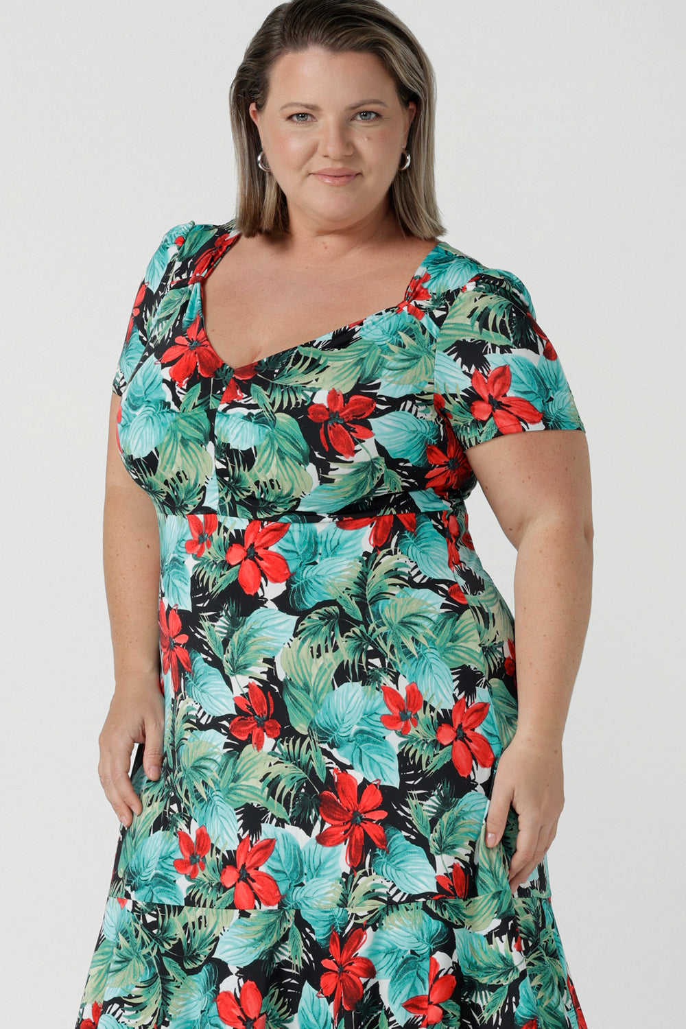 Close up of a size 18 Curvy woman wears the Jillian dress in Havana. A beautiful tropical print with a green leaf print and red flower on a white base that is tropical inspired. A sweetheart neckline style with an empire line. Tier on hem. Made in Australia for women. Size 8 - 24.