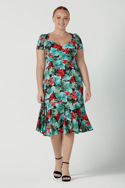 Size 12  woman wears the Jillian dress in Havana. A beautiful tropical print with a green leaf print and red flower on a white base that is tropical inspired. A sweetheart neckline style with an empire line. Tier on hem. Made in Australia for women. Size 8 - 24.