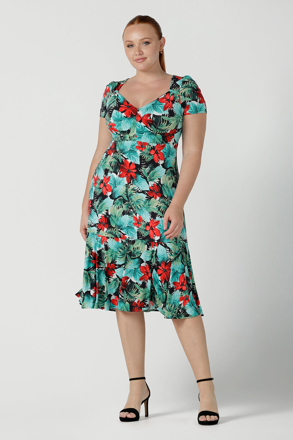 Size 12 woman wears the Jillian dress in Havana. A beautiful tropical print with a green leaf print and red flower on a white base that is tropical inspired. A sweetheart neckline style with an empire line. Tier on hem. Made in Australia for women. Size 8 - 24.