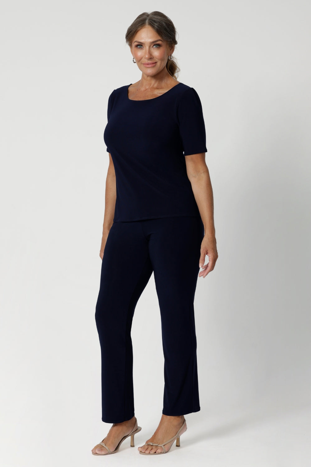 The ideal workwear pant for the combination of comfort, style, and ease. Size 12 woman wears navy workwear pants with matching navy top and a nude heel.