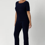 The ideal workwear pant for the combination of comfort, style, and ease. Size 12 woman wears navy workwear pants with matching navy top and a nude heel.