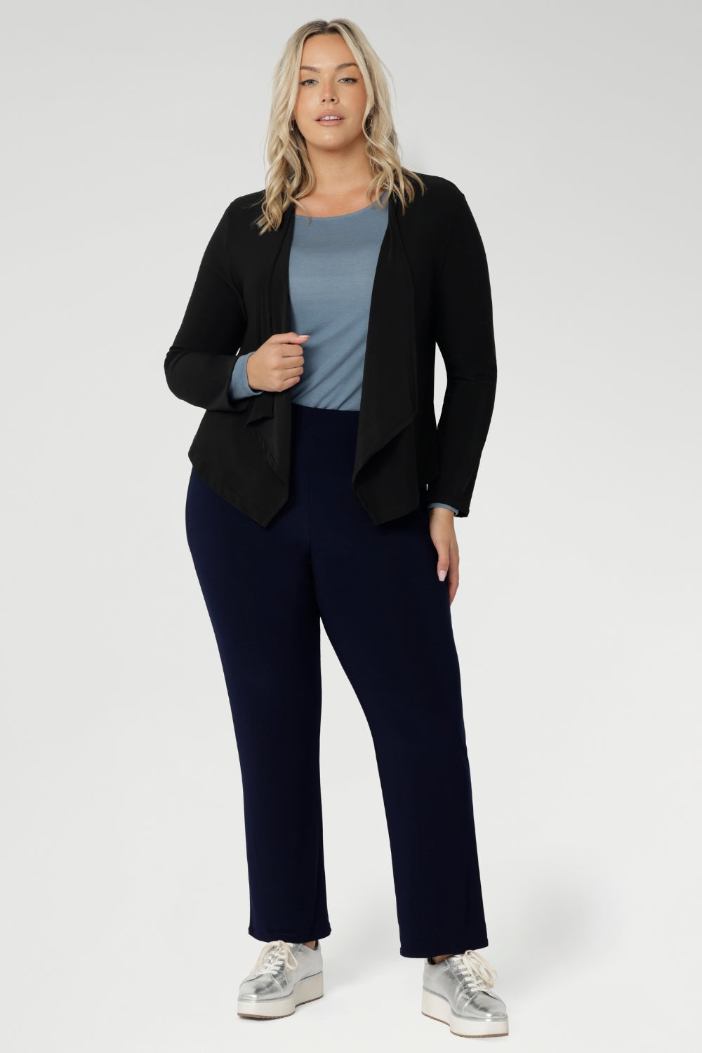 The ideal workwear pant for the combination of comfort, style, and ease. Size 18 woman wears navy workwear pants with blue blouse, black cardigan & silver sneaker.