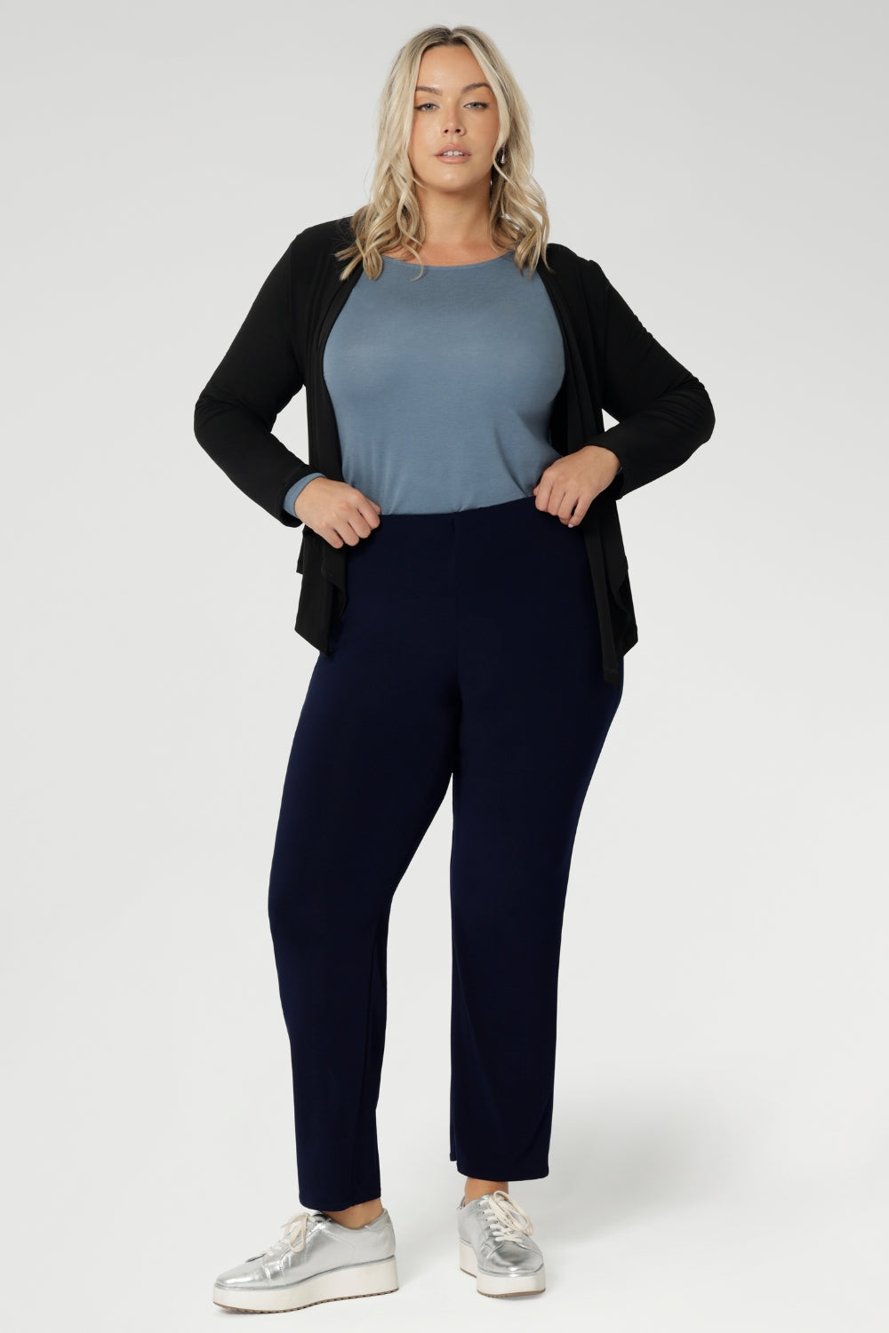 The ideal workwear pant for the combination of comfort, style, and ease. Size 18 woman wears navy workwear pants with blue blouse, black cardigan & silver sneaker.