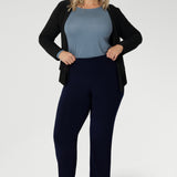 The ideal workwear pant for the combination of comfort, style, and ease. Size 18 woman wears navy workwear pants with blue blouse, black cardigan & silver sneaker.