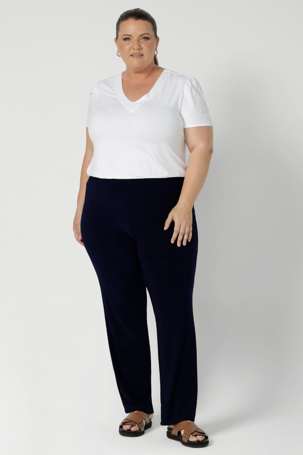 The Joel Pant is the ideal combination of comfort, style, and ease—perfect for the modern woman who values both fashion and function. Plus size woman wears navy pants with casual white tshirt & brown sandles. 