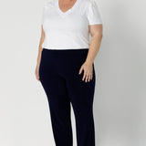 The Joel Pant is the ideal combination of comfort, style, and ease—perfect for the modern woman who values both fashion and function. Plus size woman wears navy pants with casual white tshirt & brown sandles. 