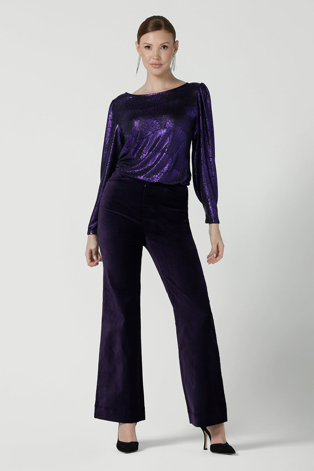 A size 10 woman wears the Zara top in purple metallic fabric. With balloon sleeves and a boat neckline. Styled back with Jonas pant in purple velveteen. The perfect cocktail suit set made in Australia for women size 8-24