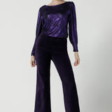 A size 10 woman wears the Zara top in purple metallic fabric. With balloon sleeves and a boat neckline. Styled back with Jonas pant in purple velveteen. The perfect cocktail suit set made in Australia for women size 8-24