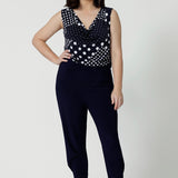 Showing a summer top for petite women, a size 12 woman wears a cowl neck jersey top. This sleeveless top has a navy and white spot print -and is worn with navy travel pants for a travel outfit look! Made in Australia by Australian and New Zealand clothing brand, Leina & Fleur, shop this top in petite to plus sizes. 