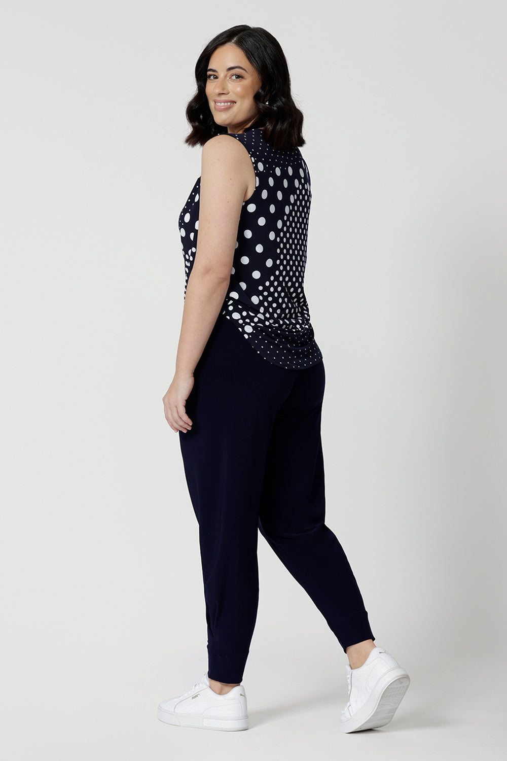 Back view of a summer top for petite women, a size 12 woman wears a cowl neck jersey top. This sleeveless top has a navy and white spot print -and is worn with navy travel pants for a travel outfit look! Made in Australia by Australian and New Zealand clothing brand, Leina & Fleur, shop this top in petite to plus sizes. 