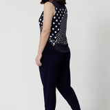 Back view of a summer top for petite women, a size 12 woman wears a cowl neck jersey top. This sleeveless top has a navy and white spot print -and is worn with navy travel pants for a travel outfit look! Made in Australia by Australian and New Zealand clothing brand, Leina & Fleur, shop this top in petite to plus sizes. 