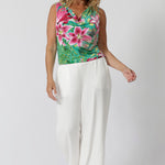 Over 40 year old woman wears resort ready stop in floral printed slinky jersey fabric. Cowl neck line adds a touch of elegance and flow. Easy care top can be dressed up or worn casually. Model pairs Joni Top with white pants to create a perfect day event look. 