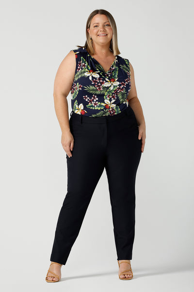 A curvy size 18 woman wears a Joni Top in Merriment print. The perfect top to wear for the Christmas festive season and on Christmas day. The top features a cowl neckline and soft stretch jersey material. Styled back with navy work pants. Made in Australia for sizes 8-24.
