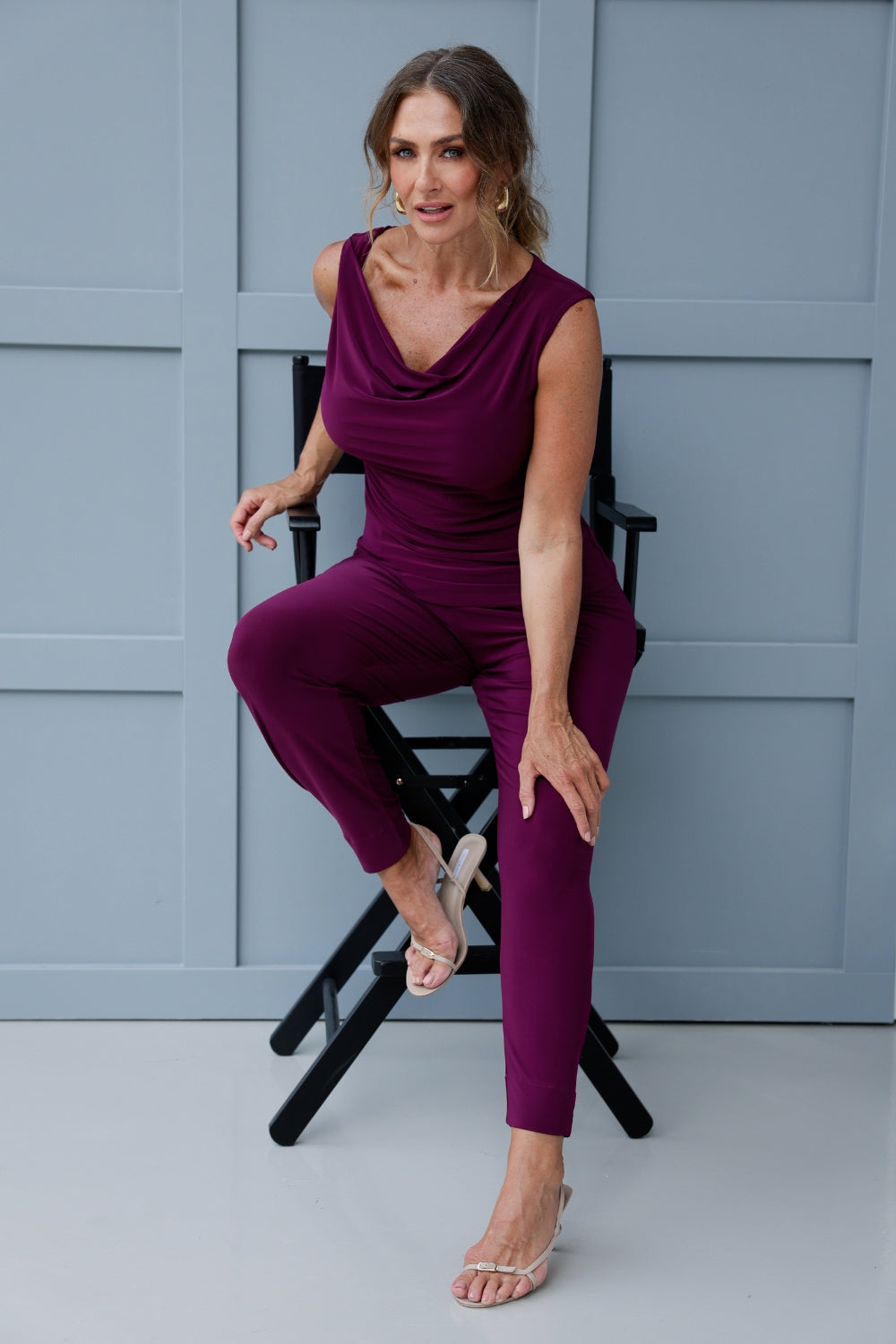 Image shows over 40's woman wearing magenta coloured top with cowl neck front, paired with matching magenta pants for a faux jumpsuit look. Reversible double-layer design can be worn with a cowl neckline front facing or flipped to reveal a boat-neck style for a more open, structured silhouette. 