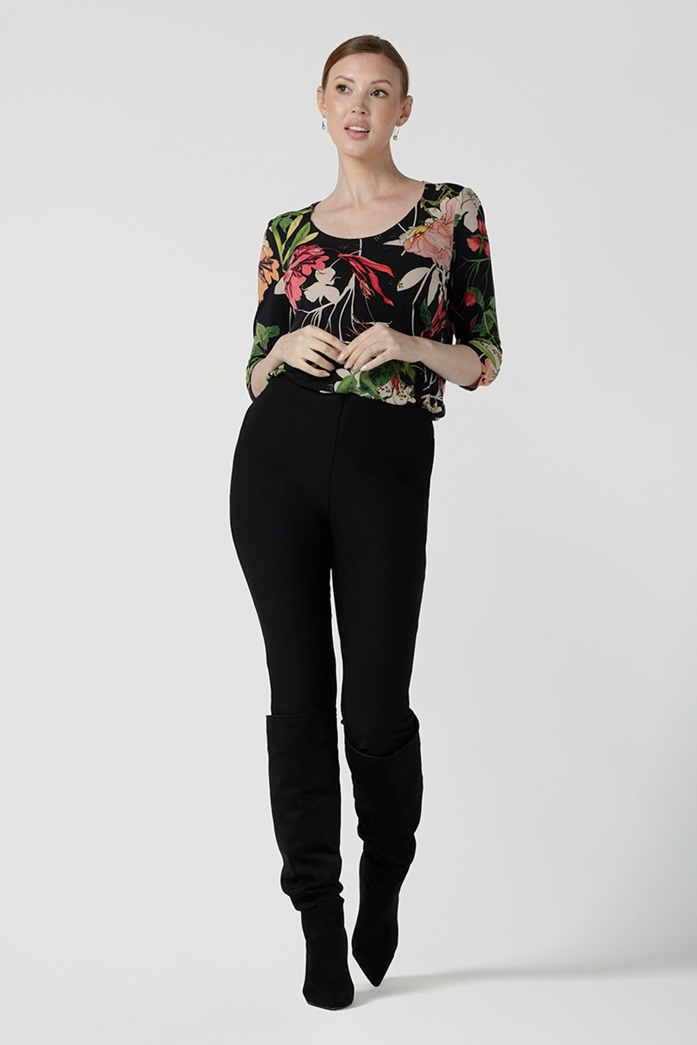 A size 10 woman wears the Jules top in Bloomsbury print. A curved neckline style with 3/4 sleeves. Made in easy care jersey fabric with a beautiful floral print with red, pink, orange, green and vanilla on a black base. Made in Australia for women size 8-24. Styled back with the slim fit Brooklyn pant in black.