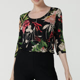 A size 10 woman wears the Jules top in Bloomsbury print. A curved neckline style with 3/4 sleeves. Made in easy care jersey fabric with a beautiful floral print with red, pink, orange, green and vanilla on  a black base. Made in Australia for women size 8-24.