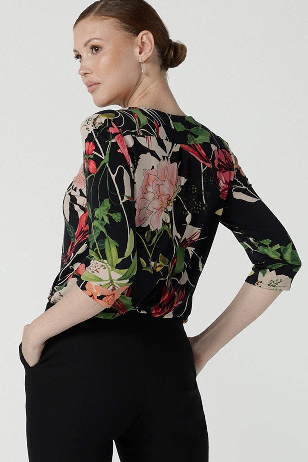 Back view of a size 10 woman wears the Jules top in Bloomsbury print. A curved neckline style with 3/4 sleeves. Made in easy care jersey fabric with a beautiful floral print with red, pink, orange, green and vanilla on a black base. Made in Australia for women size 8-24.