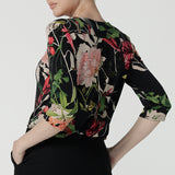 Back view of a size 10 woman wears the Jules top in Bloomsbury print. A curved neckline style with 3/4 sleeves. Made in easy care jersey fabric with a beautiful floral print with red, pink, orange, green and vanilla on a black base. Made in Australia for women size 8-24.