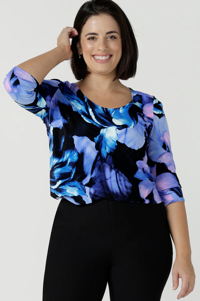 Close up of a size 10 woman wears the Jules top in Blue Lily. A Scoop neck style we a 3/4 sleeve. Digitally printed with a blue Lily Print. Size inclusive fashion, made in Australia for women size 8 - 24. Styled back with Black Brett pants.