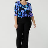 Size 10 woman wears the Jules top in Blue Lily. A Scoop neck style we a 3/4 sleeve. Digitally printed with a blue Lily Print. Size inclusive fashion, made in Australia for women size 8 - 24. Styled back with Black Brett pants. 