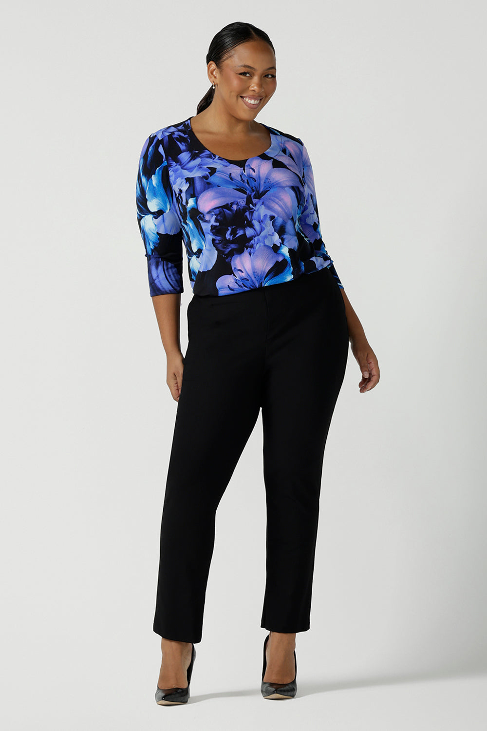 Size 16 woman wears the Jules top in Blue Lily. A Scoop neck style we a 3/4 sleeve. Digitally printed with a blue Lily Print. Size inclusive fashion, made in Australia for women size 8 - 24. Styled back with Black slim leg brooklyn pants. 