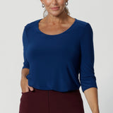 The Jules Top is the ultimate collarless tailored shirt, designed for both workwear and weekend wear. Crafted from a deep blue dry-touch jersey fabric, round neck top offers a soft stretch that moves with you, ensuring all-day comfort without compromising on style. Size 12 woman pairs her Jules top with wine coloured workwear trousers. 