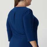 Back view image of plus size woman shows her wearing deep blue workwear top showcasing back shoulder yoke with a central pleat below that provides extra shape and dimension, enhancing the top’s tailored feel. Available in sizes 8-24. 