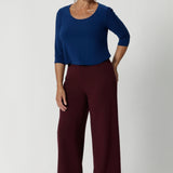 Image shows over 40's woman wearing a 
women's basic tailored shirt. Designed for both workwear and weekend wear. Crafted from a deep blue dry-touch jersey fabric, this top offers a soft stretch that moves with you, ensuring all-day comfort without compromising on style. Easy care workwear top provides a polished finish with it's wrinkle resistant qualities. Available in sizes 8-24, online at Leina & Fleur. 