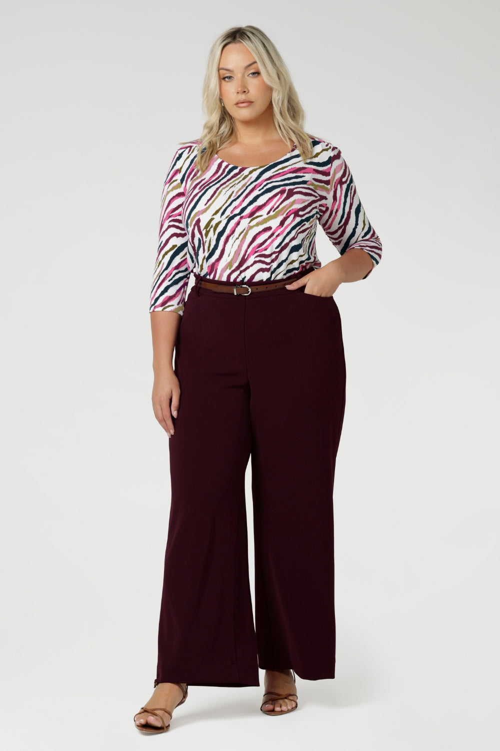 The shirttail hemline adds versatility, making it perfect for both tucked-in and untucked styling. Size 18 model wears her workwear shirt tucked into wine coloured tailored pants, paired with a brown belt and heel.