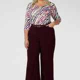 The shirttail hemline adds versatility, making it perfect for both tucked-in and untucked styling. Size 18 model wears her workwear shirt tucked into wine coloured tailored pants, paired with a brown belt and heel.