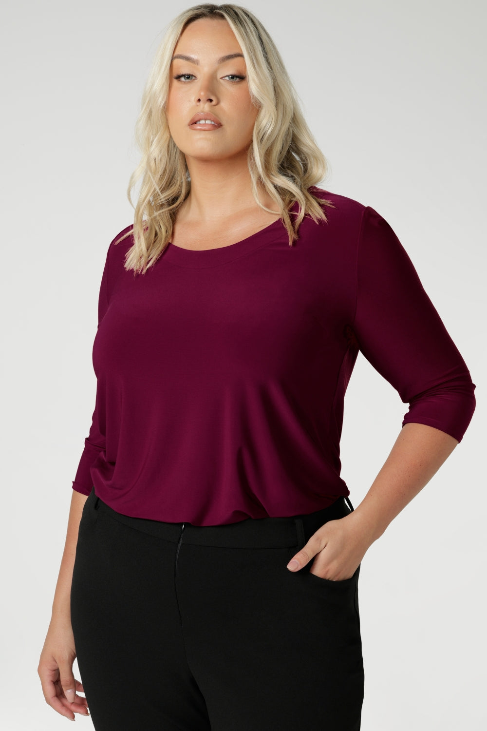 The shirttail hemline adds versatility, making it perfect for both tucked-in and untucked styling. Whether worn under a suit for a polished office look or paired with casual pieces for the weekend, the Jules Top effortlessly transitions with your schedule. Size 18 woman wears her top tucked into black workwear pants.